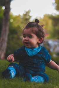 Cute toddler girl in a blue outfit sitting on grass, smiling outdoors.