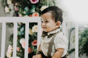 Charming baby boy dressed elegantly with a bowtie, surrounded by colorful flowers.