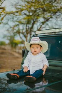 Charming baby boy sitting on a car hood wearing a cowboy hat, capturing innocence and style.