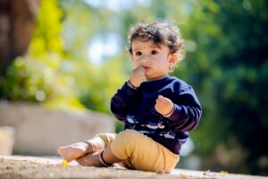 Cute child sitting in a park on a sunny day in Malegaon, India, surrounded by green leaves.