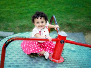 Adorable child in a polka dot dress plays joyfully on a merry-go-round outdoors.