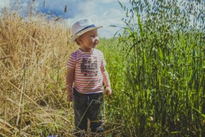 A happy child wearing a straw hat enjoying a sunny day in a green field, surrounded by nature.