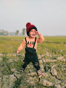 A crying baby boy stands in a field in Sukkur, Sindh, Pakistan.