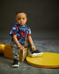 Charming toddler wearing a vibrant shirt and sneakers, sitting indoors.