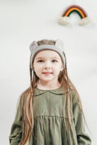 Charming portrait of a young girl in a green dress with a cute headband, smiling indoors.