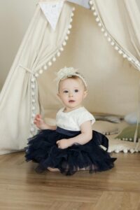 Cute baby sits in a navy tutu inside a tent, perfectly capturing innocence and charm.
