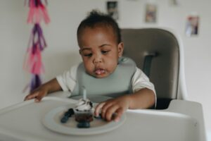 Adorable baby in high chair savoring a cupcake with a candle. Celebratory mood indoors.