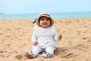 Cute baby girl in a sun hat enjoying a sunny day sitting on the sandy beach.