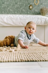 Charming baby boy crawling on indoor rug, intrigued by wooden toys, in a cozy home setting.