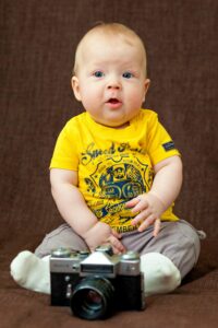 Charming baby boy in bright attire seated with a classic camera in a studio.